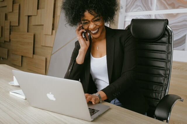 An elegant woman wearing a business suit, seated at a desk and using a laptop.