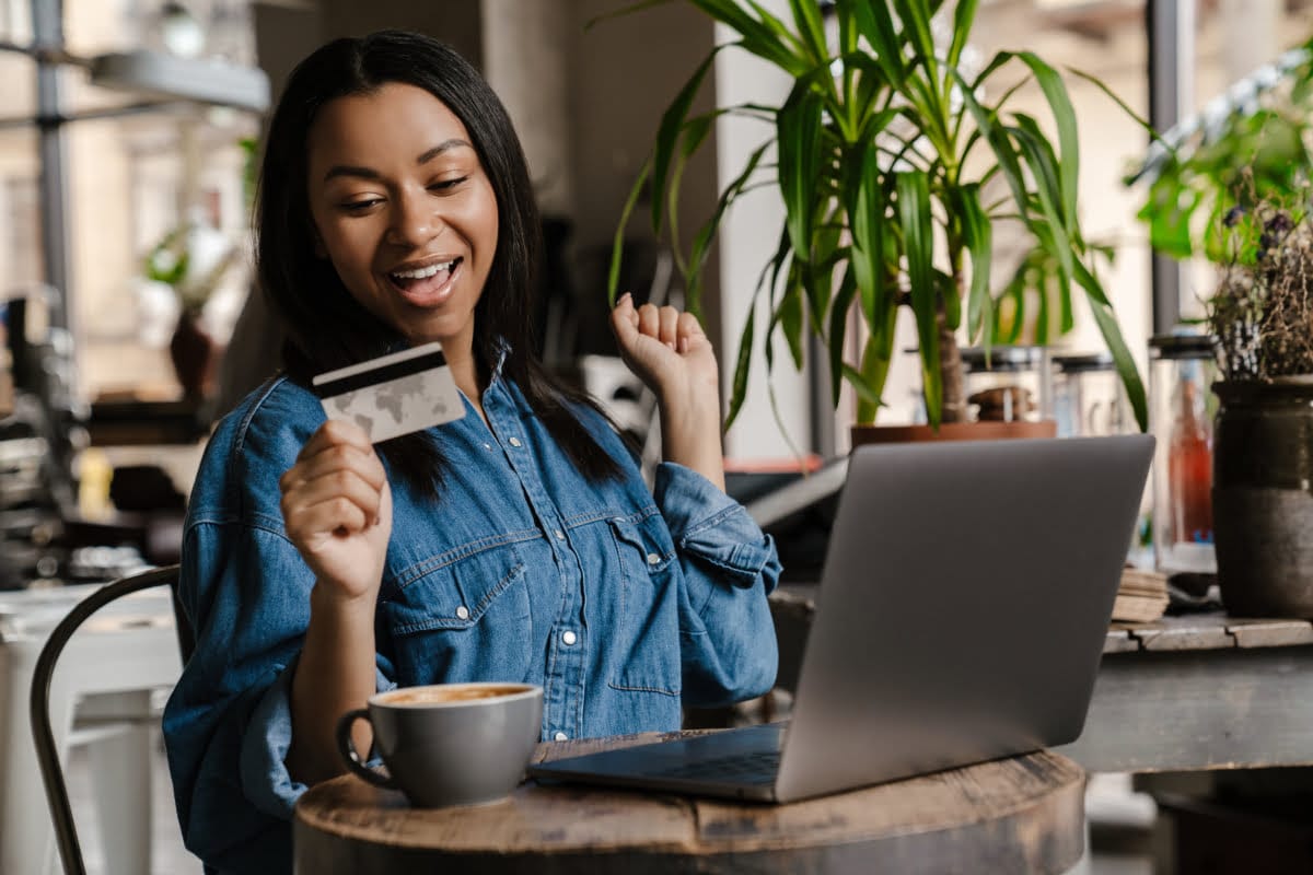 A woman holding a credit card while sitting at a table in a coffee shop.