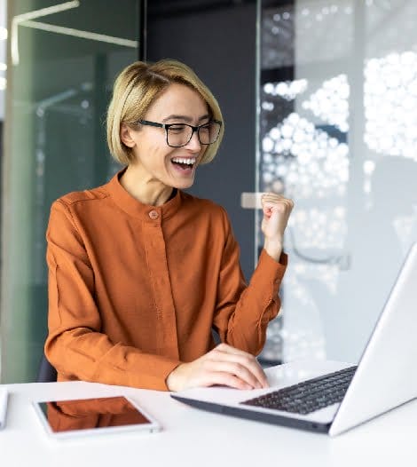 A woman wearing glasses sits at a desk, using a laptop and holding a credit card for online transactions.