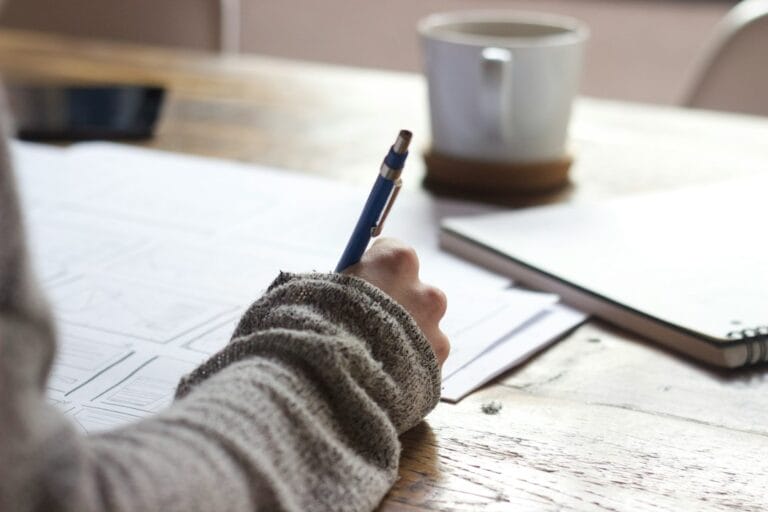 A person writing on a piece of paper at a desk.