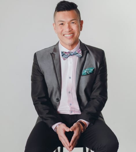 A well-dressed man in a suit and bow tie sitting on a chair.