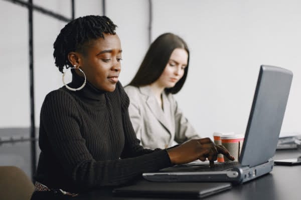 Two women sitting at a table, focused on their laptops, engaged in work or study.