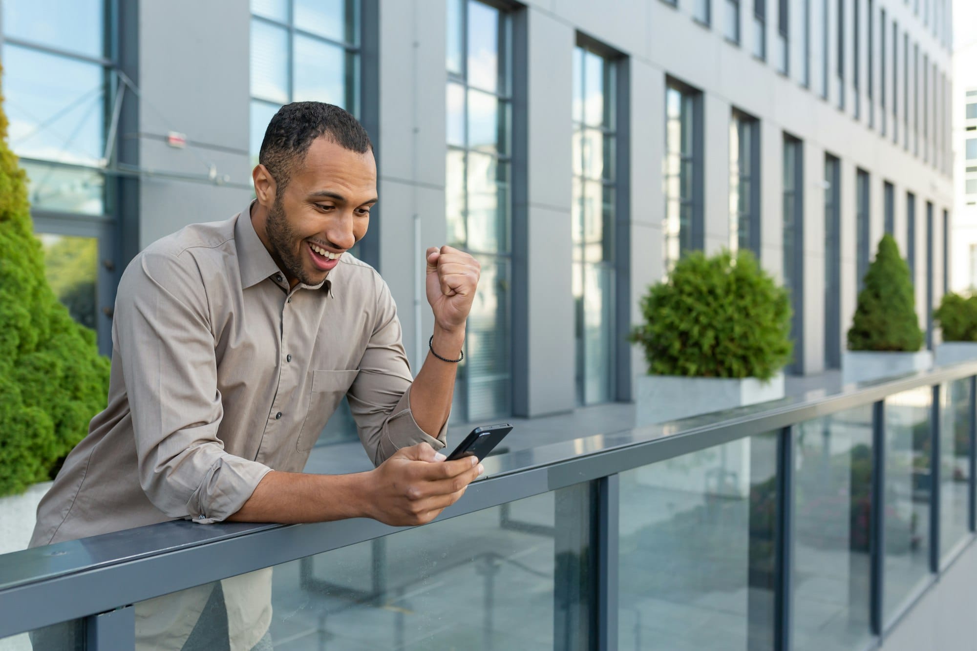 A happy Hispanic businessman standing near the office. Holding phone, playing online games